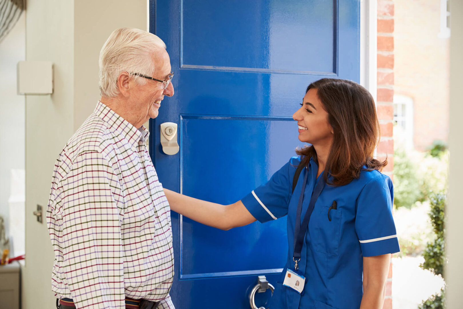 A nurse is greeting an older man outside of the door.