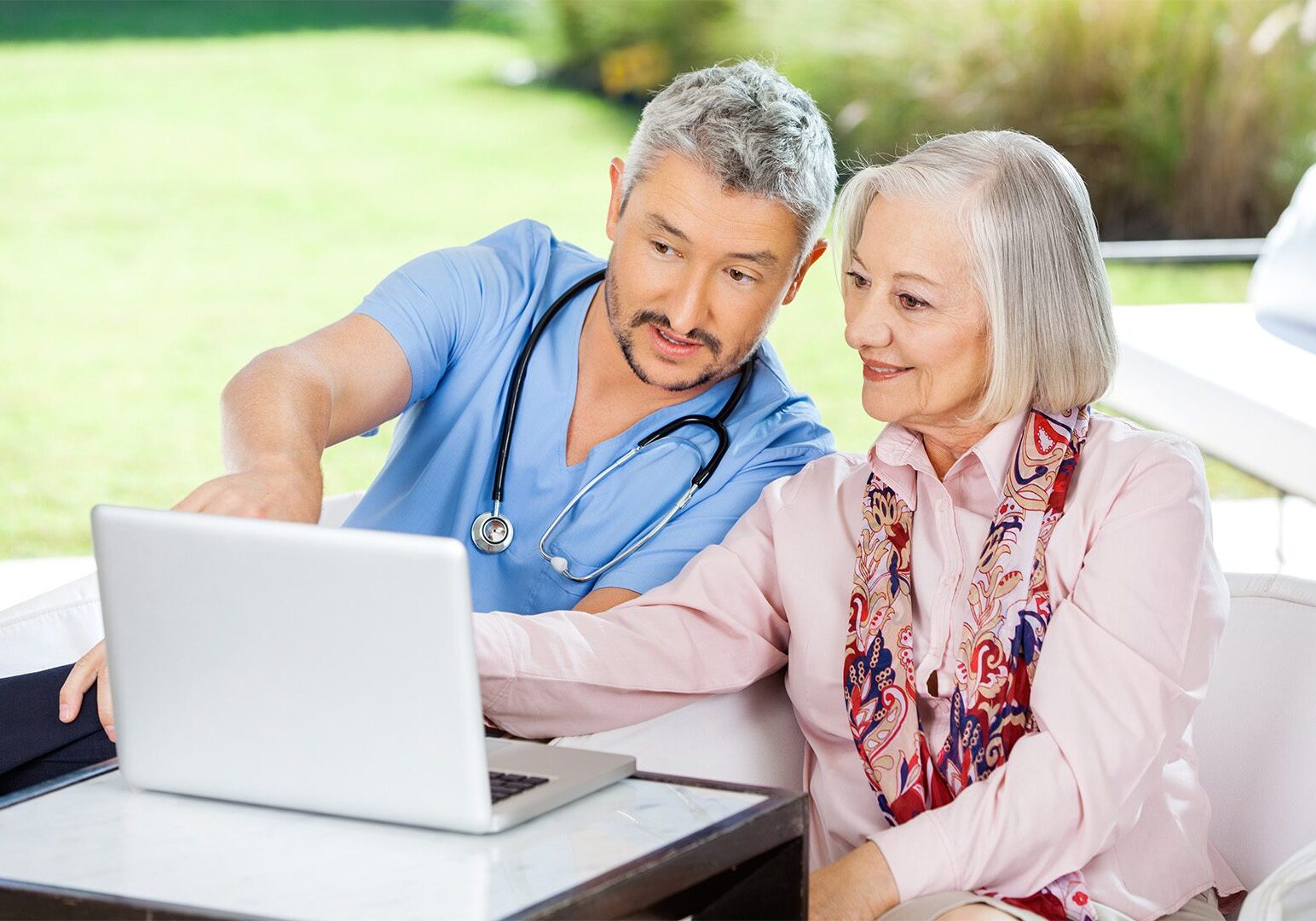 Male caretaker assisting senior woman in using laptop at nursing home porch